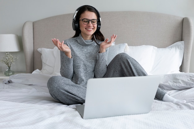 Donna sorridente del colpo pieno che lavora con il computer portatile in camera da letto