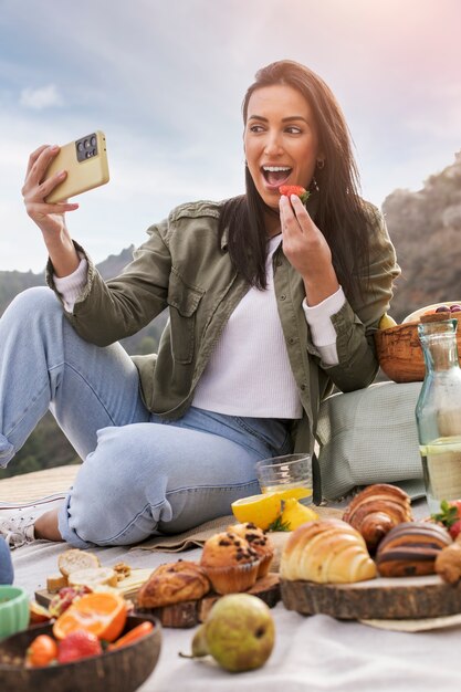 Donna sorridente del colpo pieno che prende selfie mentre mangia