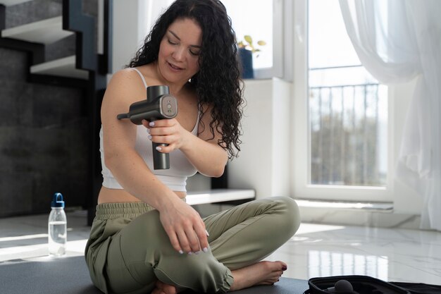 Donna sorridente del colpo pieno che utilizza la pistola di massaggio