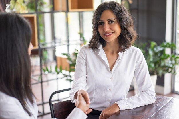 Donna sorridente di affari che agita le mani con il socio in caffè.