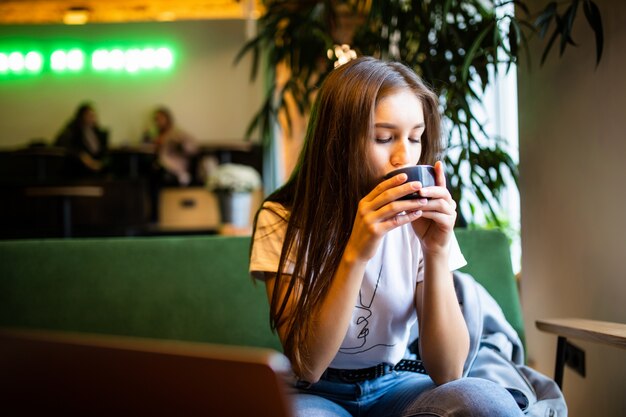 Donna sorridente di buon umore con la tazza di caffè che si siede nella caffetteria.