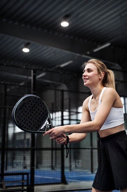 Donna sorridente di vista laterale che gioca a paddle tennis