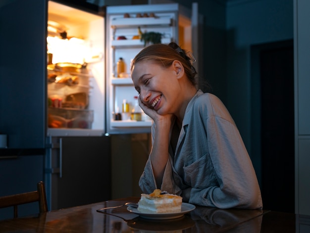 Donna sorridente di vista laterale che mangia spuntini di notte