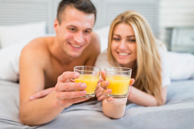 Donna sorridente e uomo con bicchieri di succo nel letto