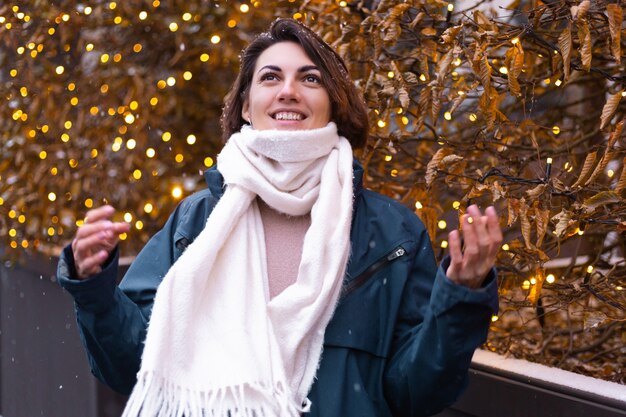 Donna sorridente felice caucasica che gode della neve e dell'inverno, indossando sciarpa calda
