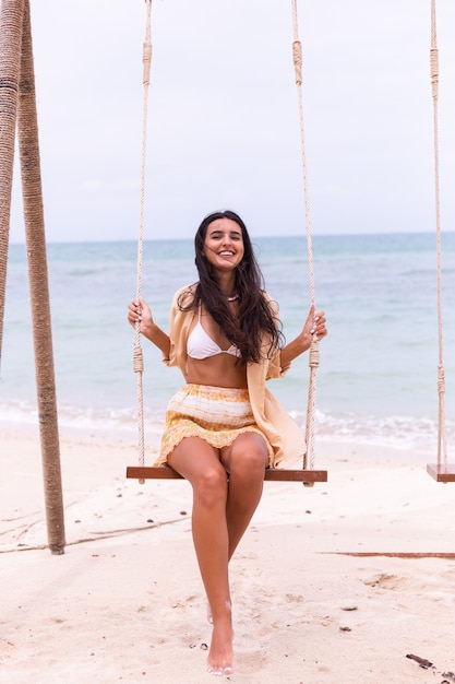 Donna sorridente felice su oscillazione in spiaggia, luce calda del giorno.