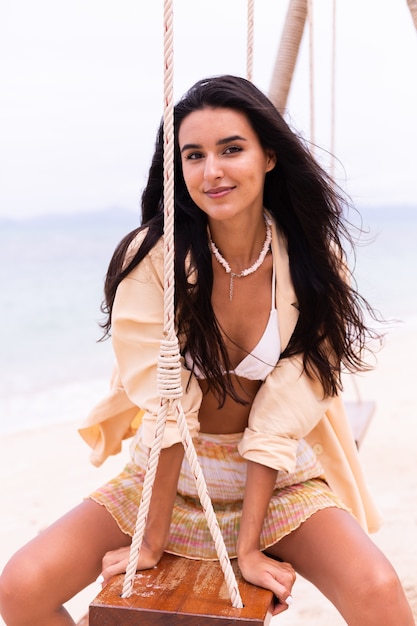 Donna sorridente felice su oscillazione in spiaggia, luce calda del giorno.