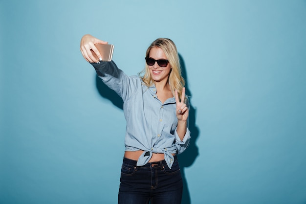 Donna sorridente in camicia e occhiali da sole che fanno selfie sullo smartphone