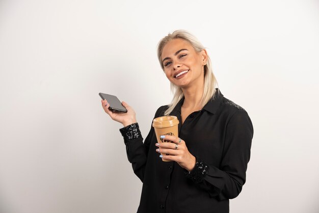 Donna sorridente in piedi con il telefono cellulare e la tazza di caffè. Foto di alta qualità