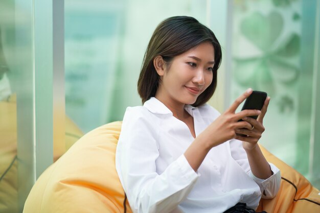 Donna sorridente in sedia Beanbag utilizzando smartphone