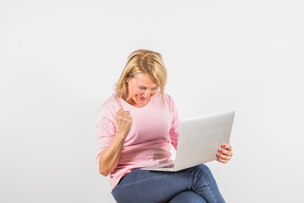 Donna sorridente invecchiata in camicetta rosa con laptop e pugno chiuso