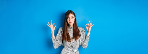 Donna sorridente non male soddisfatta con i capelli lunghi che indossa un abito che mostra segni ok e sembra soddisfatta