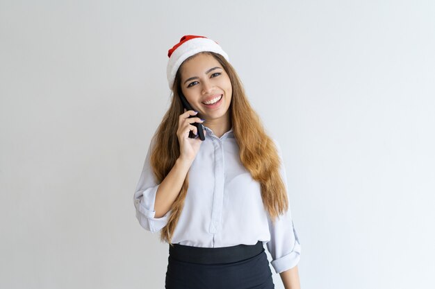 Donna sorridente parlando su smartphone e indossa il cappello di Babbo Natale