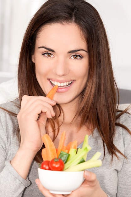 Donna sorridente sul divano a mangiare insalata di verdure