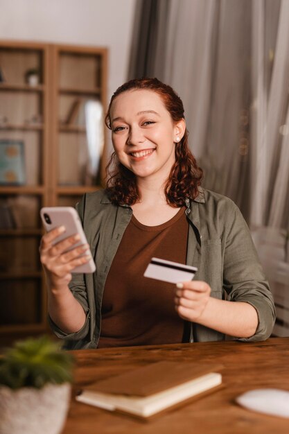 Donna sorridente utilizzando carta di credito e smartphone a casa