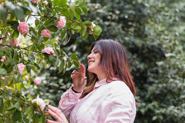 Donna sorridente vicino a molti fiori rosa che crescono sui ramoscelli verdi