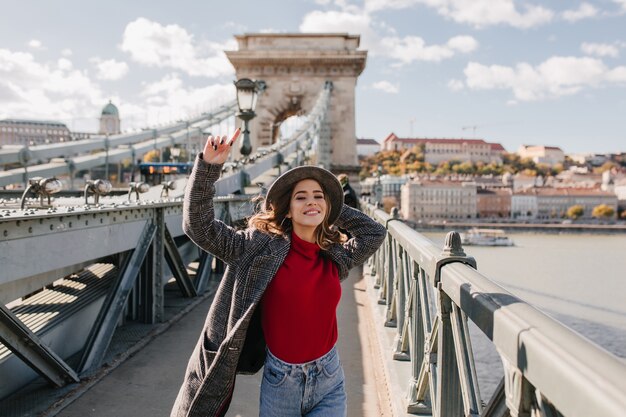 Donna spensierata in maglione rosso casual, godersi la vita e in posa sullo sfondo della città