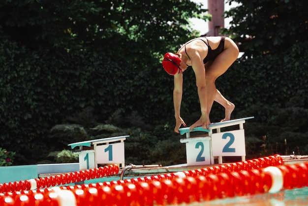 Donna sportiva che indossa un costume da bagno nero che si prepara per iniziare a nuotare in una piscina pubblica all'aperto