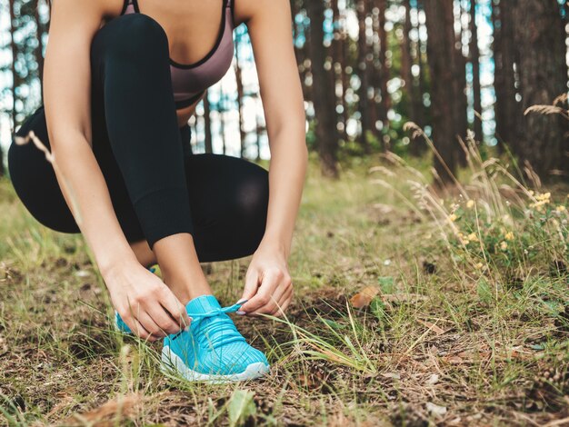 Donna sportiva che lega i lacci delle scarpe sulle scarpe da corsa prima dell'allenamento nella foresta