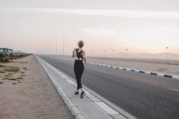 Donna straordinaria motivata dal retro in esecuzione su strada nella mattina di sole. Allenamento, allenamento, emozioni vere, stile di vita sano, laboriosa, forte sportiva, paese tropicale.