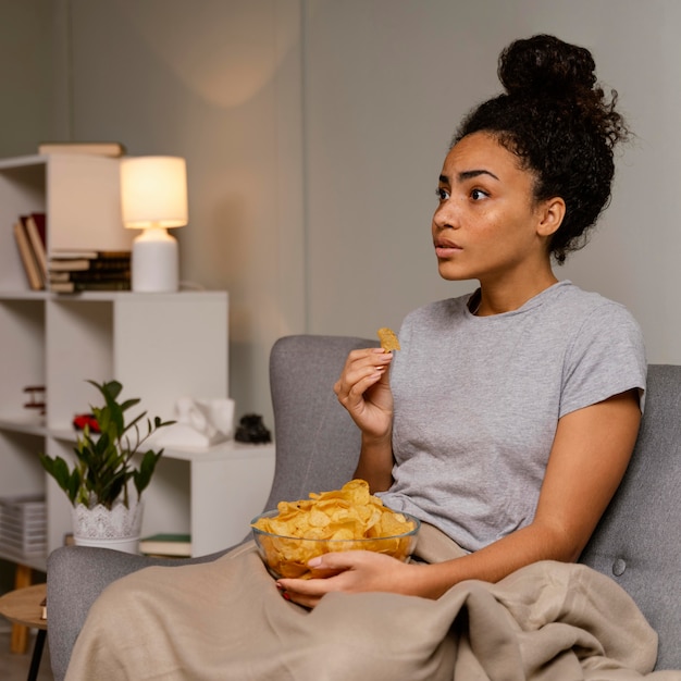 Donna sul divano a guardare la tv e mangiare patatine