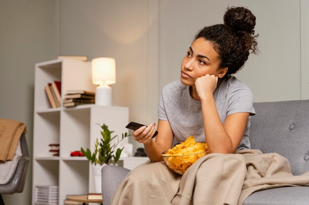 Donna sul divano a guardare la tv e mangiare patatine