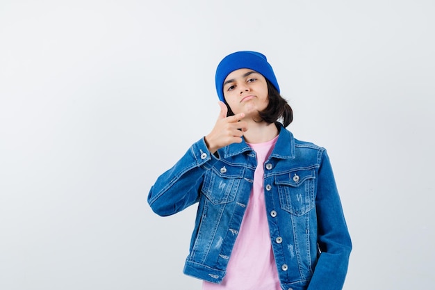 Donna teenager che indica alla macchina fotografica in berretto rosa della giacca di jeans della maglietta che sembra carino