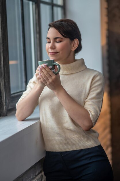 Donna tranquilla e rilassata che inala l'aroma del caffè