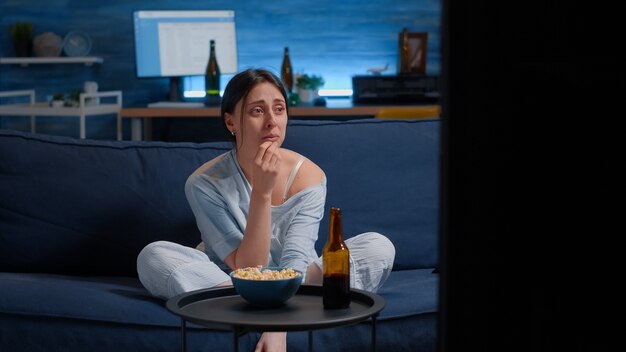 Donna triste che piange guardando un film drammatico in tv seduto sul divano mangiando popcorn