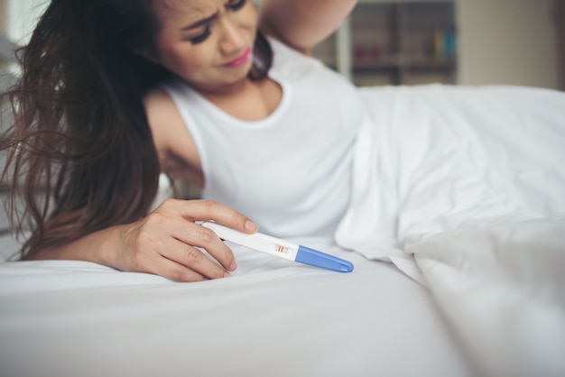 Donna triste che si lamenta tenendo un test di gravidanza che si siede sul letto