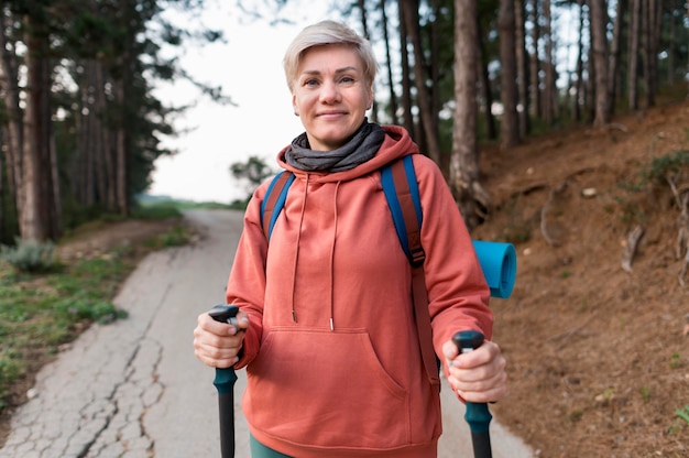 Donna turistica senior di smiley con i bastoni d'escursione nella foresta