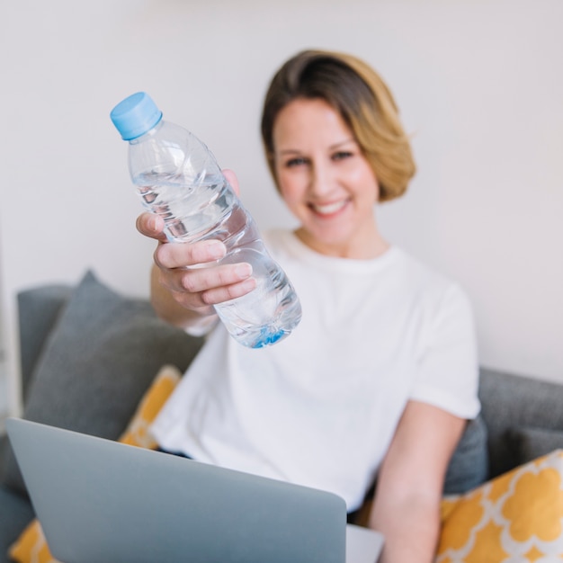 Donna vaga con il computer portatile che mostra bottiglia di acqua