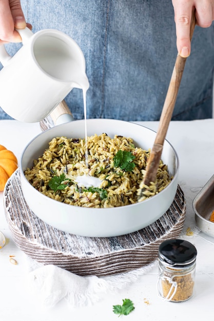 Donna versando il latte di cocco su riso al curry e coriandolo