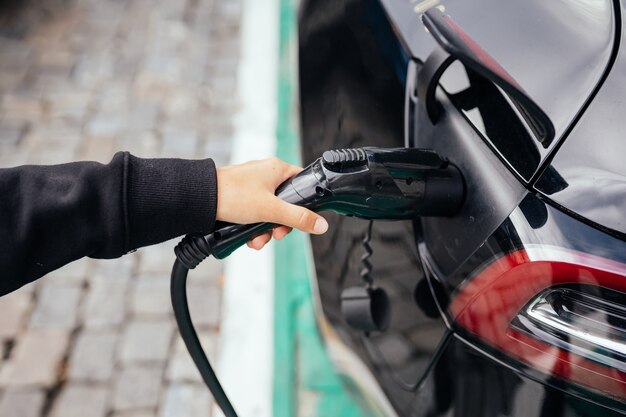 Donna vicino all'auto elettrica. Veicolo caricato alla stazione di ricarica.