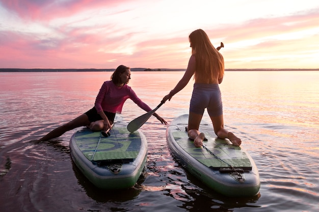 Donne a tutto campo che fanno paddleboarding al tramonto
