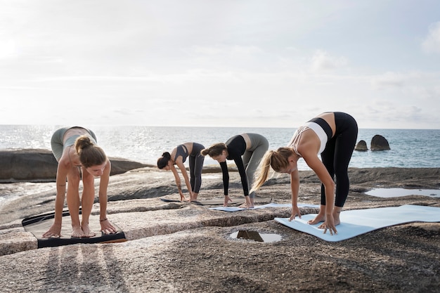 Donne a tutto campo che si esercitano sulla stuoia di yoga in riva al mare
