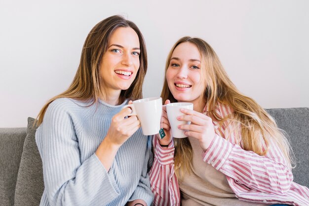 Donne adorabili con le tazze che esaminano macchina fotografica