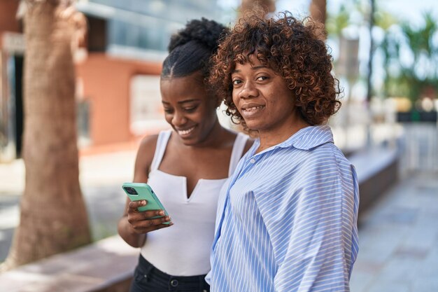 Donne afroamericane madre e figlia che utilizzano smartphone in strada