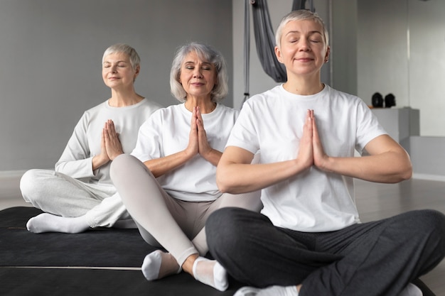 Donne anziane che fanno esercizi di yoga in palestra su stuoie di yoga