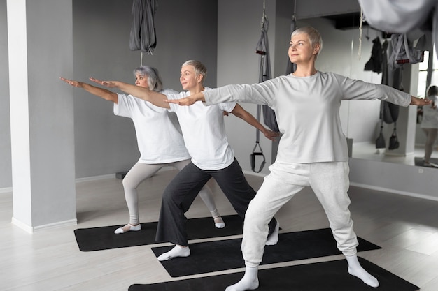 Donne anziane che fanno esercizi di yoga in palestra su stuoie di yoga