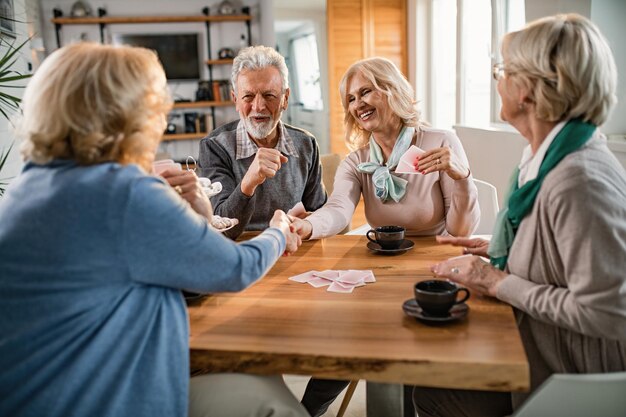 Donne anziane felici che si stringono la mano dopo aver giocato a carte con i loro amici a casa