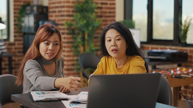 Donne asiatiche che guardano lo schermo del laptop per ricercare informazioni finanziarie, scambiare idee per pianificare una nuova strategia aziendale per lo sviluppo e la crescita. Team di persone che utilizzano le statistiche al lavoro.