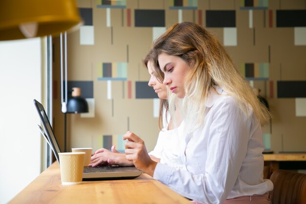 Donne caucasiche che lavorano su laptop e bevono caffè da asporto