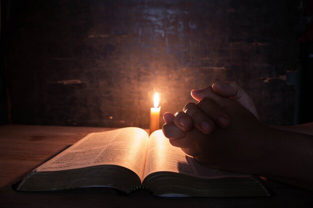 donne che pregano sulla Bibbia nel fuoco selettivo delle candele leggere.
