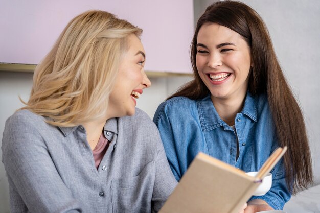 Donne che ridono felici che mangiano caffè e libro di lettura