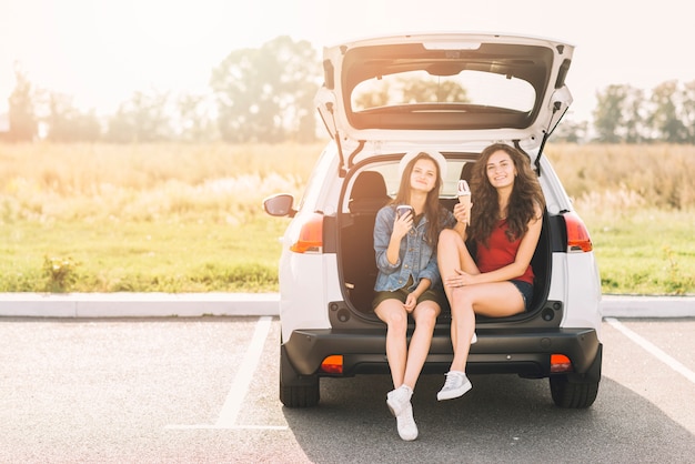 Donne che si siedono sul bagagliaio dell&#39;auto con il gelato