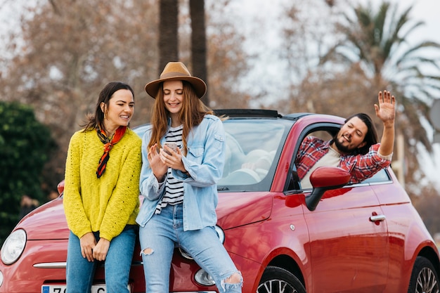 Donne con smartphone vicino a uomo sporgendosi dalla macchina