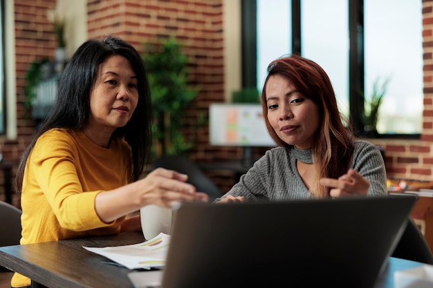 Donne d'affari che lavorano al progetto di gestione che analizzano le statistiche sul computer portatile idee di brainstorming durante la riunione di lavoro nell'ufficio di avvio. Dirigenti esecutivi che collaborano insieme