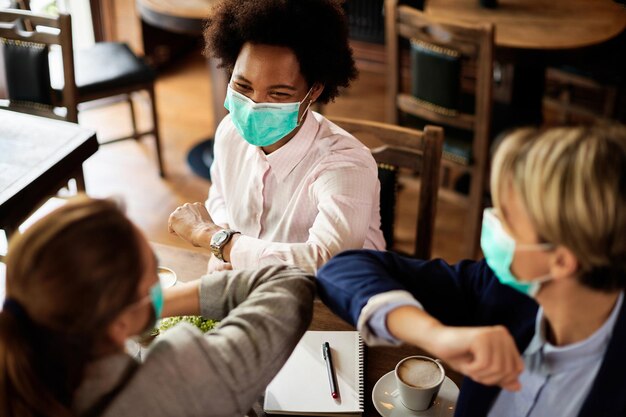 Donne d'affari felici con maschere facciali che urtano il gomito in un caffè