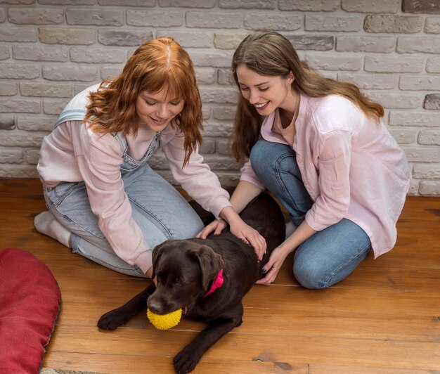 Donne del colpo pieno che giocano con il cane sul pavimento